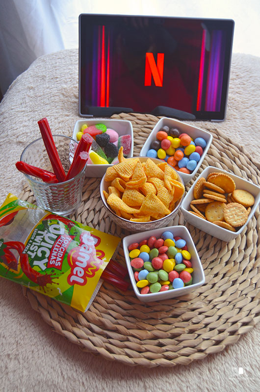 Mesa de snacks para noche de cine en casa con cuencos de palomitas, chuches y decoración acogedora.