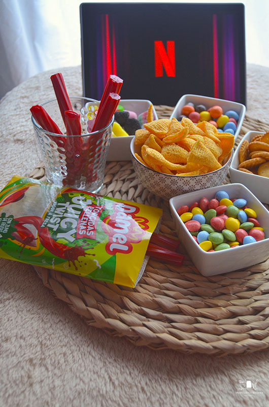 Mesa de snacks para noche de cine en casa con cuencos de palomitas, chuches y decoración acogedora.