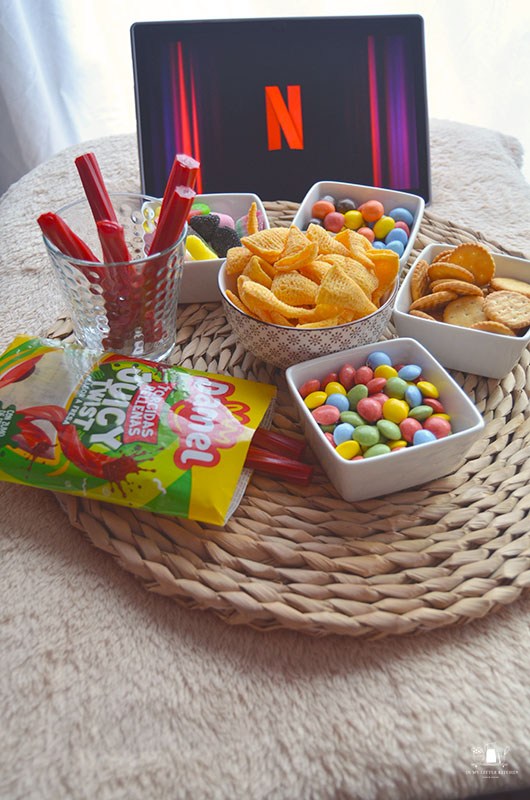 Mesa de snacks para noche de cine en casa con cuencos de palomitas, chuches y decoración acogedora.